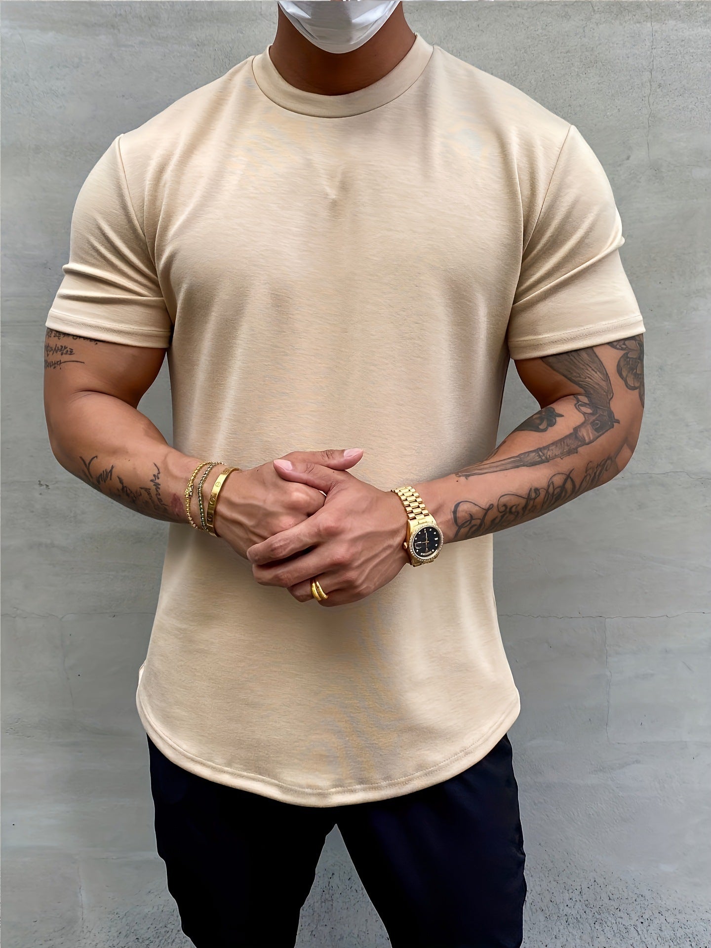 Person wearing a beige t-shirt and dark pants against a gray background