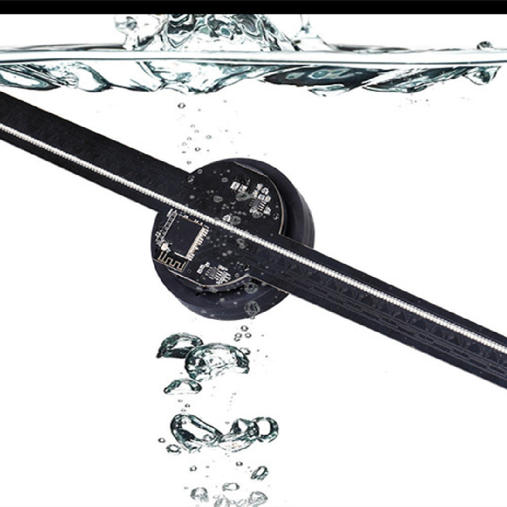 Black zipper with a small round device attached, partially submerged in water with bubbles.