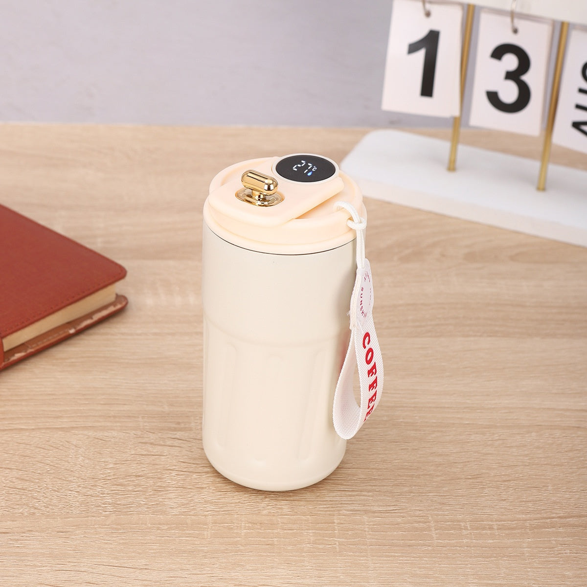 White ceramic mug with gold lid on a wooden surface, featuring a 'Coffee' tag.