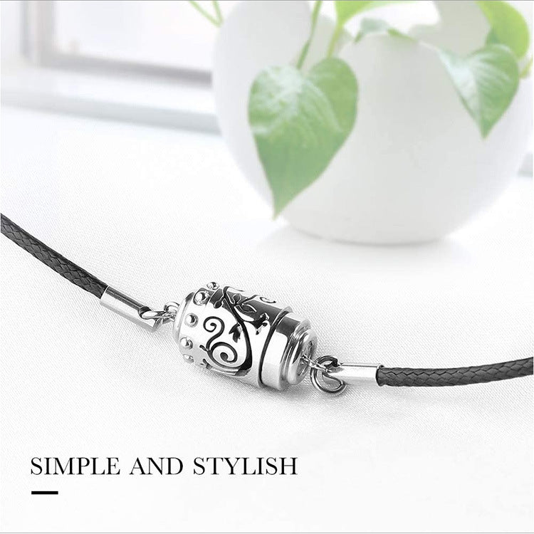 Silver pendant on a black cord with a white background and green plant