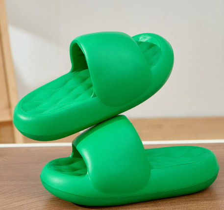 Green slippers stacked on a wooden floor with a neutral background