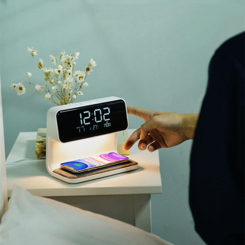 Smart clock with phone charging station on a nightstand, with a hand interacting with it.