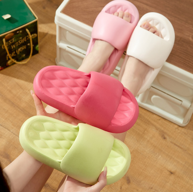 Three pairs of colorful slippers held by a hand on a wooden floor.
