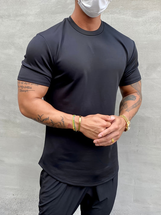Person wearing a black t-shirt and pants with tattoos on arms, standing against a gray background.